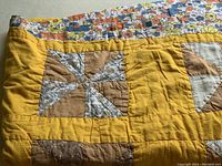 Close-up photo showing the pinwheel patchwork design with solid and floral fabric pieces, mustard yellow border.