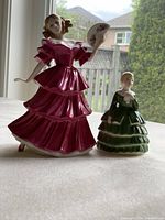 Front and side view of two Royal Doulton figurines Jennifer and Belle placed on a white surface with outdoor background