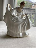 Front view of the Royal Doulton Pamela figurine showing the woman holding her flowing dress with detailed facial features and blue trim on her dress.