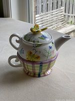 Composite image showing ceramic teapot with butterfly lid and cup stacked together.
