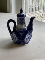 Side view of dark blue patterned ceramic teapot with lid on, showing handle, spout, and decorative pattern.
