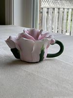 Miniature rose-shaped teapot body with detailed petals and green handle on white surface near window