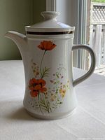 Porcelain teapot with orange poppy floral pattern, lid on, showing spout, handle, and overall shape.
