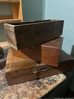 Three wooden boxes stacked, top open box showing dovetail joinery dark wood, middle medium brown open box, bottom lidded box with latch.