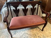 Front view of antique wooden settee with pink fabric seat placed on rug.