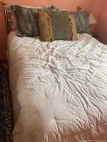 Full view of double bed with white comforter, decorative pillows, brass headboard visible
