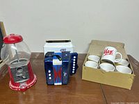 Photo shows the red and clear bubble gum machine along with the mini accordion and a box containing six Max coffee mugs.