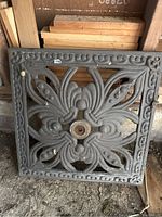 Square cast iron decorative panel showing intricate floral design with a central hole.