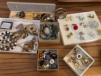 Top view of assorted costume jewelry including clip-on earrings, bracelets, necklaces and brooches in boxes and trays.