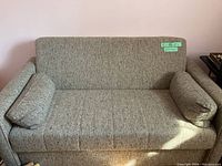 Front view of gray upholstered pull out couch with two cylindrical arm cushions, showing texture and condition of fabric.