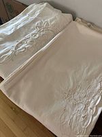 Folded linen pieces including duvet cover, bed skirt, and pillow shams showing detailed embroidery and fabric texture.