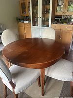 Assembled round table with leaf in place surrounded by four chairs against cabinetry backdrop