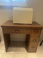 Singer sewing machine in a white hard case placed on wooden sewing machine table cabinet