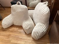 Two white plush vertical ribbed support cushions with handles shown on wooden floor.