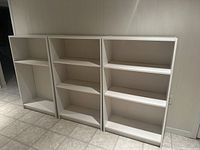 Photo of three white bookcases standing side by side, showing front view including shelves and overall structure.