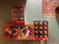 Photo showing three boxed sets of vintage Christmas ornaments: one box of 8 Holiday Living ornaments with purple and gold glitter, and two other boxes with assorted spherical ornaments in a variety of colors and detailed patterns.