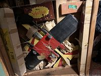 Top view of two partially built vintage model airplanes, predominantly red, black, and yellow, showing metal wire structures and wheels with balsa wood components and paper stuffing inside a crate.