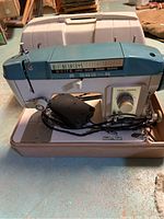 Front angle view showing entire sewing machine in beige case with foot pedal placed on base.