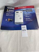 Photo of original packaging and identification tag, showing the First Alert branding, product name, and features such as battery backup and plug-in operation.