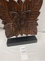 Shows front angle view of one abstract wooden sculpture with a carved flower and leaf design on a black base.