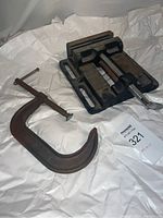 Two heavy duty drill press vises and a rusty large C-clamp seen on white background fabric.