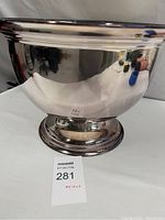 Front and side view of the polished stainless steel ice bucket cooler showing its reflective surface and round base.