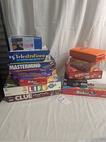 Stack of eleven boxed games including puzzle and classic board games on a white surface with curtain background.