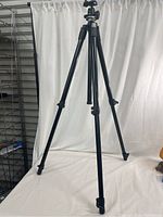 Full view of the extended black tripod standing on a white sheet with visible tripod legs and clamps.
