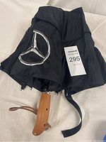 Folded black umbrella showing the Mercedes Benz star logo and wooden handle with wrist strap.