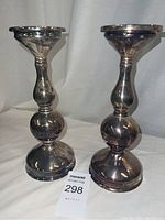 Photo showing two silver tone candle stick holders side by side on white cloth.