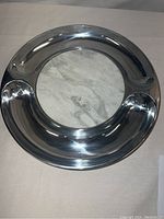 Top view of round serving tray showing shiny silver-tone outer metal alloy ring with two indentations and central white marble insert with natural veining.