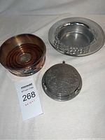 Three silver plated items: two wine bottle holders and one coaster with grapevine embossed lid, placed on white background.