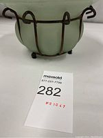 Photo of vintage green blown glass vase with iron cage frame, showing base and iron feet.