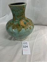 Green glazed ceramic vase with brown drip accents shown upright on white cloth background with auction tag