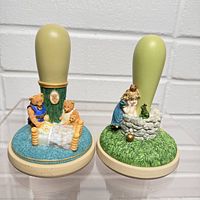 Two cookie press molds showing detailed figurine handles of teddy bears and a girl with a frog at a well.