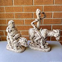 Front view of Don Quixote and Sancho Panza decorative figures placed against a brick wall background.