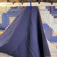Image showing the back of the quilt as solid dark blue fabric with quilting stitches visible.