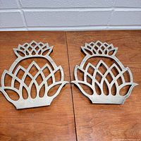 Front view of two metal pineapple-shaped silverplate trivets on wood surface showing their size and design