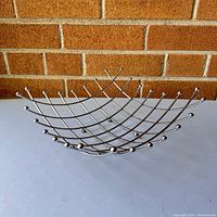 Front view of modern chrome wire fruit basket on table with brick wall background.
