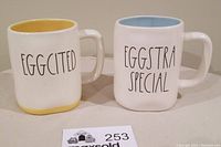 Front view of two Rae Dunn mugs with 'EGGCITED' and 'EGGSTRA SPECIAL' text showing their front sides and handles.