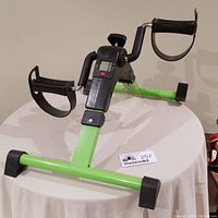 Full view of the bright green under desk exercise bike showing frame, foot pedals with straps, and digital display.