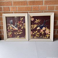Full view of both framed bird prints with floral branches against brick background