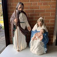 Mary, Joseph, and baby Jesus Christmas blow mold figures displayed together on a white table in front of a brick wall.