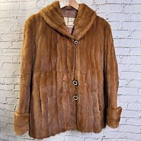 Full front view of vintage Eaton's medium brown fur ladies coat, jacket length on a hanger against a brick wall backdrop.