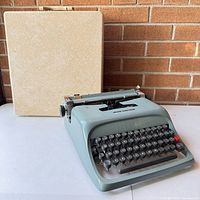 Olivetti Underwood Studio 44 typewriter outside case on table against brick wall background.