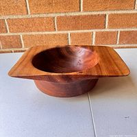 Front angled view showing the carved wooden bowl with its rounded interior and square rim, wood grain details visible.