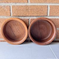 Front view of two round teak wooden bowls placed side by side showing interior surfaces with natural grain and color variation.