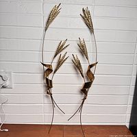 Pair of metal wire sheaves of wheat wall art pieces hung on a white brick wall showing full length and shape