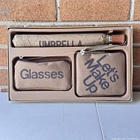 Open box showing umbrella, glasses case, and makeup case in beige packaging with clear view of text labels.
