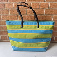 Front view of the striped tote bag showing blue, green and yellow horizontal stripes and black handles.